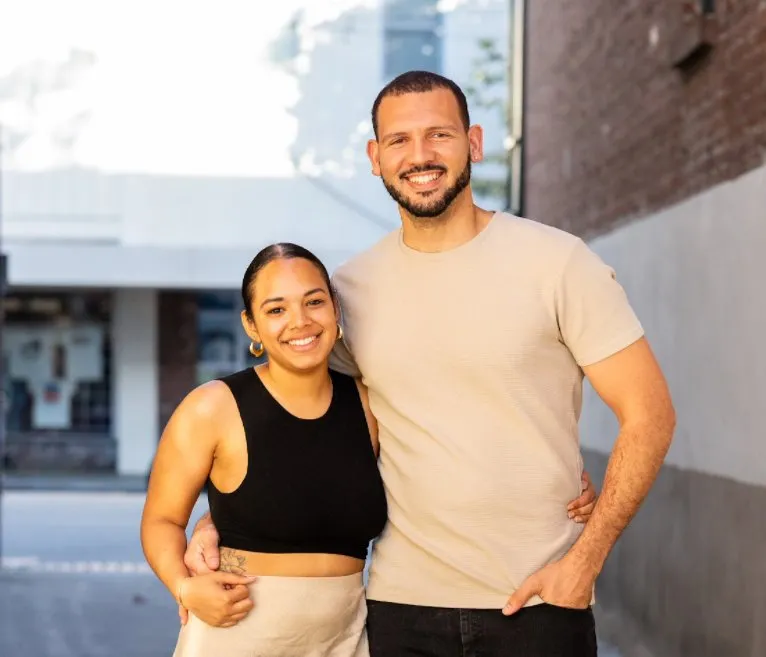 Jordan and Melina smiling with their arms around each other on a city street